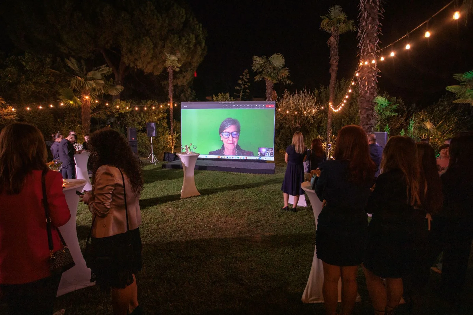 Guests in an evening garden watching a screen during the anniversary event