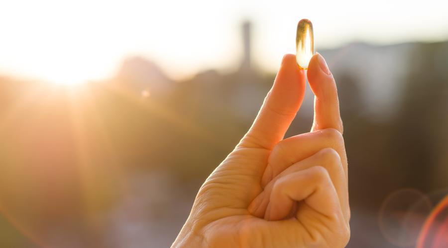 Hand of a woman holding fish oil Omega-3 capsules, urban sunset background